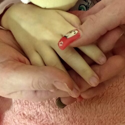Hände eines Erwachsenen halten eine Kinderhand mit rot verzierten Nägeln.