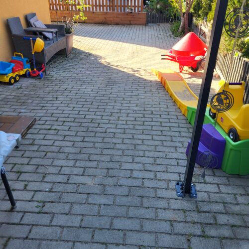 Sonniger Hof mit Pflaster, roter Schubkarre und buntem Kinderspielzeug