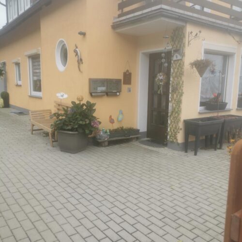 Gelbes Haus mit Balkon und Holztuer, Hofpflaster und Blumenbeeten, ruhig